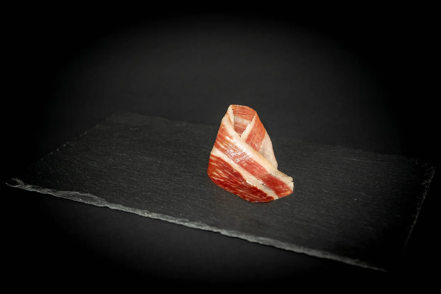 Lonchas de jamón presentadas sobre una pizarra oscura